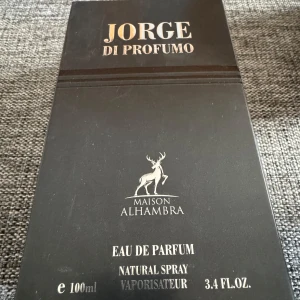 Jorge di Profumo Maison Alhambra - Jorge di Profumo från Maison Alhambra är en Eau de Parfum för män med fräscha, kryddiga och aromatiska toner. Flaskan är svart med silverdetaljer och rymmer 100 ml. Doften har inslag av citrus, lavendel, trä, tobak och varma kryddor. Perfekt för dig som gillar maskulina och unika dofter. Plasten är borttagen, men helt oanvänd.