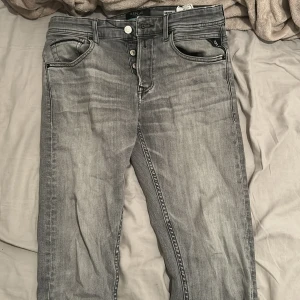 Replay Grover grå jeans straight fit - Snygga Replay Grover jeans i en tvättad grå färg med straight fit. Klassisk femficksmodell, svarta detaljer på bakfickorna och tydlig Replay-label bak. Jeansen har knappgylf och är tillverkade i jeansmaterial med en cool, lite sliten look. Storlek W29 L32
