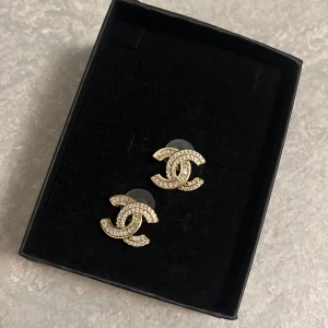 Glittriga örhängen i CC-motiv - Guldfärgade örhängen med CC-motiv i rostfritt material. Endast testade