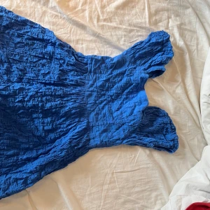 Blå omlottklänning från mango  - Säljer en blå omlottklänning från mango  med snyggt rynkad struktur och breda axelband. Klänningen har en öppen rygg och är tillverkad i mjuk bomull, perfekt för varma dagar. Modellen är kort och har en loose passform som ger en chill vibe.