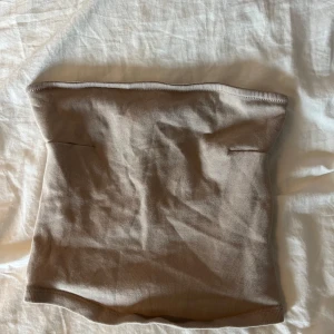 Beige ribbad tubtopp från Gina Tricot - Säljer en beige ribbad tubtopp från Gina Tricot i storlek XS. Toppen är axelbandslös och har en enkel, stilren design som är lätt att matcha. Perfekt för varma dagar eller lager på lager-stil.