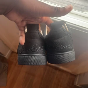 Svarta sneakers från Christian Louboutin storlek 40 41 - Säljer ett par svarta sneakers från Christian Louboutin med klassisk röd sula och signatur på undersidan. Skorna har snörning, rund tå och är tillverkade i mocka med en ganska ren platt sula. Perfekt för dig som gillar exklusiva detaljer och vill sticka ut med något unikt.