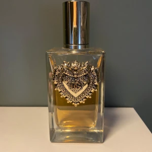 Dolce & Gabbana Devotion EdP 100ml - Lyxig parfymflaska från Dolce & Gabbana, Devotion Eau de Parfum, 100 ml. Flaskan är rektangulär i tjockt, genomskinligt glas med guldig vätska och dekorerad med ett detaljerat hjärtemblem i metall och DG-logga. Snygg metallkork som ger exklusiv känsla. Använd flera gånger så att det finns ungefär 75ml i flaska nu. Saknas original kartong eftersom har slängt det. 