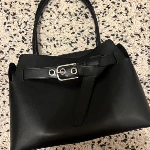 Hm Totebag  - En totebag i ytbehandlad kvalitet med tubformade handtag som kan fästas samman med hjälp av en slejf med metallspänne. Lång rem runt överdelen med öljetter och metallspänne. Fodrad. Djup 15 cm. Höjd 25 cm. Bredd 35 cm. Elegant och snygg ( säljs inte längre på Hm) köptes för två månader sen användes inte alls mycket och det märks på bilderna ☺️