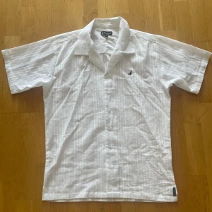 Vit skjorta från Blanc du Nil i linne - Vit kortärmad skjorta från Blanc du Nil i luftig linnemix. Skjortan har diskreta vertikala ränder, klassisk krage och knäppning framtill. Liten svart logga broderad på bröstet. Perfekt för varma dagar och en clean look. Passar en som är emellan 170-185. Hör av vid intresse/ funderingar! 