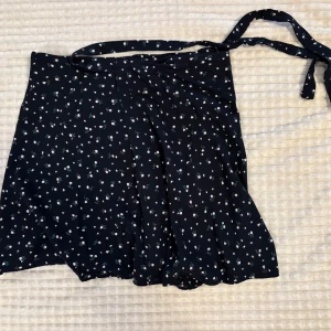 Kjol från Brandy Melville - Supersöt svart omlottkjol från Brandy Melville med små rosa och vita blommor. Kjolen har knytband i midjan. Inga defekter. 