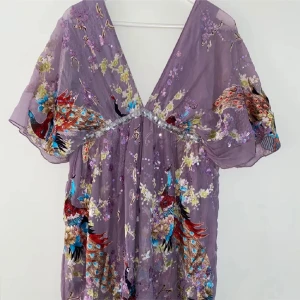 Lila blommig kortklänning med paljetter - Vacker kort paljettklänning som jag fått så många fina komplimanger för! Äkta silke. Märke Traffic People, nypris 1900kr! Syrenlila botten med otroligt fint påfågelmotiv. Dragkedja på sidan, silkeslen och skön underklänning. Fin till fest och bröllop!👌