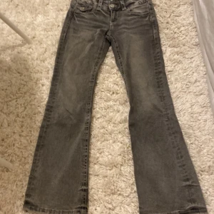 Grå bootcut jeans Gina Tricot 146 - Snygga grå jeans från Gina Tricot i bootcut-modell. Jeansen har coola detaljer med broderade bakfickor och dekorativa knappar. Materialet är klassisk denim och passformen är normal med utsvängda ben. Perfekta för dig som gillar en fin vibe.