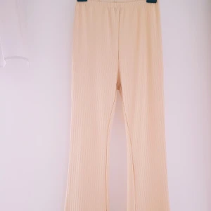 Beiga ribbade utsvängda byxor från SHEIN strl M - Snygga beiga byxor från SHEIN i ribbat material med elastisk midja. Byxorna har raka, vida ben och är superbekväma med en avslappnad passform. Perfekta för en chill och stilren look.  Trådsläpp vid muddarna vid fötterna annars helt & fint skick