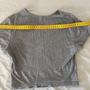 Grå croppad t-shirt från Tna - Säljer en enkel och stilren grå croppad t-shirt från Tna. T-shirten har korta ärmar, rund halsringning och är tillverkad i mjuk bomull. Perfekt att matcha med höga jeans eller shorts för en avslappnad look.