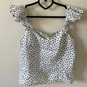 Prickig linnetopp med volangaxlar - Supersöt vit linnetopp med blå prickar och volangiga axelband. Banden är insydda så passar S/M!🌸🌸