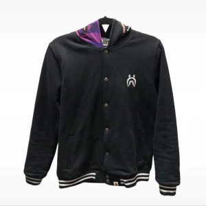 BAPE svart bomberjacka med camo-huva - Svart bomberjacka från BAPE - Det Japanska A Bathing Ape med ikonisk haj- och camo-huva i lila och detaljerade broderade bokstäver. Jackan har tryckknappar, randiga muddar och två fickor. Yttertyg i bomull,m. Perfekt för dig som vill sticka ut med streetwear. Väldigt fin skick!