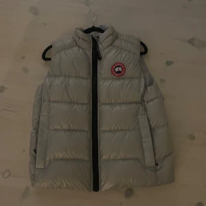 Silver dunväst från Canada Goose - Snygg silver väst från canada goose. Västen är använd 1 gång och nya priset var kring 500€, alltså kring 5600 kronor. Den är i perfekt skick och är storlek S.