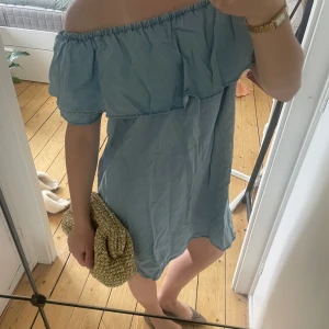 Ljusblå offshoulder kortklänning - Supersöt ljusblå kortklänning med offshoulder och volang upptill. Klänningen har en avslappnad passform och är perfekt för varma dagar. Tillverkad i ett mjukt bomullsliknande material som känns skönt mot huden.