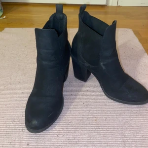 Svarta boots med klack - Snygga svarta boots med hög klack och rund tå. Skorna har en resår på sidorna. Materialet är i mocka. Använda fåtal gånger så skorna är i bra skick 
