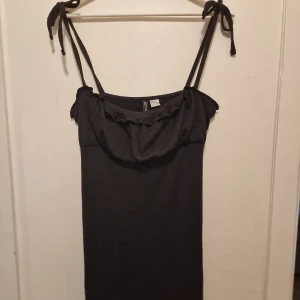 Svart romantisk klänning - Supersöt svart klänning med tunna axelband och volangdetalj vid bysten. Sitter snyggt och är lätt att styla till olika tillfällen.