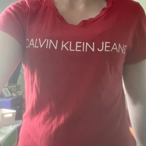 Röd Calvin Klein Jeans t-shirt - Snygg röd t-shirt från Calvin Klein Jeans med vit logga tryckt över bröstet. Klassisk passform med korta ärmar och rund halsringning. Perfekt för en clean och stilren look. Materialet är mjuk bomull som känns skönt mot huden.