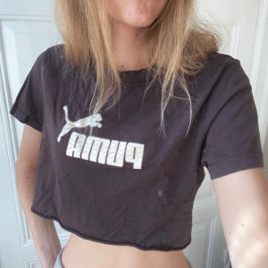 Brun croppad t-shirt från Puma - Brun croppad t-shirt från Puma med klassisk logga i vitt framtill. T-shirten är klippt croppad. 