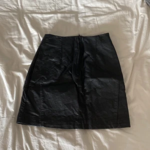 Svart skinnkjol från H&M Divided - Snygg svart kort skinnkjol från H&M Divided i storlek 32. Kjolen har en rak passform, markerade sömmar och dragkedja fram. Perfekt för dig som gillar en edgy stil och vill ha en klassisk bas i garderoben. Säljer för att den är förliten.
