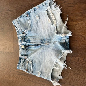 Ljusa jeansshorts från Zara - Snygga ljusblå jeansshorts från Zara med fransiga kanter och slitna detaljer både fram och bak. Klassisk femficksmodell med dragkedja och knapp. Storlek 34