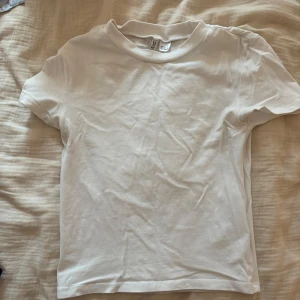 Vit basic t-shirt från H&M Divided - Enkel och stilren vit t-shirt från H&M Divided. Klassisk rund halsringning och korta ärmar. Perfekt att matcha med jeans eller kjol för en clean look. Tillverkad i mjuk bomull som känns skön mot huden.