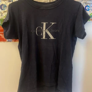 Svart Calvin Klein Jeans t-shirt - Svart t-shirt från Calvin Klein Jeans med stort CK-tryck i vitt på bröstet. Klassisk rund halsringning och korta ärmar. Tillverkad i 100% bomull för en skön och avslappnad känsla. Perfekt för dig som gillar stilrena loggoplagg.