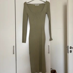 Ribbad grön långklänning från NA-KD - Snygg ribbad långklänning från NA-KD i en ljusgrön nyans. Klänningen har lång ärm, fyrkantig ringning och figurnära passform. Perfekt för dig som gillar stilrena och trendiga plagg med enkel design. Den har en slits på sidan.