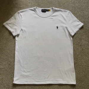 Ralph lauren T-shirt vit - Riktigt snygg vit T-shirt med blått märke från Ralph lauren, tyget är lite grövre än deras vanliga tröjor men garanterar att denna är lika skön att ha på dig, skick: 10/10 Inga defekter. Storlek S, hör av er vid frågor🤗 Mvh