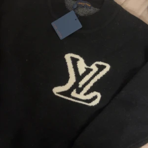 Svart stickad tröja  - Svart stickad tröja från  med stort vitt framtill. Klassisk rund halsringning och ribbade muddar. Perfekt för dig som vill ha en exklusiv och stilren look med streetvibe.