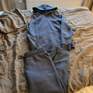 Björn Borg  - Snygg blå Tracksuit från Björn Borg med dragsko i midjan och diskret logga på benet. Byxorna har en relaxed fit och är tillverkade i mjukt bomullsmaterial, perfekta för chill dagar eller när du vill vara bekväm. Tröjan är i ett skönt material och sitter perfekt på din kropp. Både bekväm och snygg! 