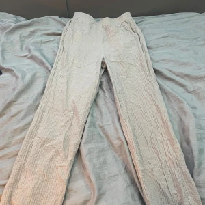 Beige linnebyxor från Grunt, M - Luftiga och sköna beige linnebyxor från Grunt i storlek M. Byxorna har rak passform, resår i midjan och är tillverkade i ett mjukt, strukturerat linnematerial. Perfekta för en chill och avslappnad stil.