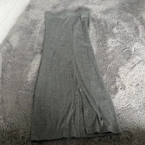 Grå ribbad långkjol Xoxo & Friends - Snygg grå ribbad långkjol från Xoxo & Friends. Kjolen har en rak passform och en diskret slits på sidan som ger extra rörelsefrihet. Perfekt för dig som gillar en enkel men stilren look.