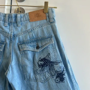 BDG ljusblå cargojeans med brodyr - Jättecoola BDG jeans från Urban outfiters inte används ofta.  W 26, L 32, men lite uppfållade. För ref jag är 165 och de slutar precis vid golvet med skor på .