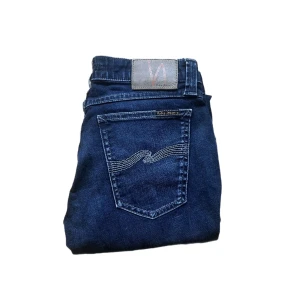Nudie jeans  - Snygga mörkblå jeans från Nudie med klassisk femficksdesign och ikonisk vågstickning på bakfickorna. Modellen är skinny fit med smala ben och normal midja. Tillverkade i mjukt jeansmaterial som sitter tajt men bekvämt. Längd 101cm. Jag skickar ej bild när jag bär plaggen och jag vet ej vilken längd och vikt de passar då jag inte prövar kläderna jag säljer 😃