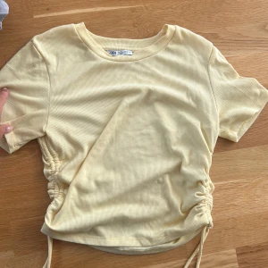Ljusgul ribbad topp från zara storlek L - Superfin ljusgul ribbad topp från H&M med korta ärmar och snörning i sidorna för en snygg, justerbar passform. Perfekt för dig som gillar en enkel men trendig stil. Mjuk och skön bomullskänsla. Liten i storleken