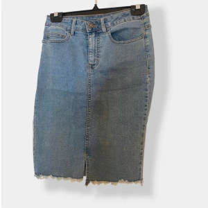 Blå jeanskjol från Noisy May - Snygg blå jeanskjol från Noisy May i klassisk modell med fem fickor och rå, fransig kant nertill. Kjolen har en liten slits framtill och är perfekt för dig som gillar en avslappnad och trendig stil.