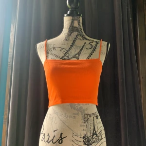 Orange croppad linne  - Superfräsch orange croppad linne från Gina Tricot med tunna axelband och ribbad struktur. Perfekt för varma dagar när du vill sticka ut med en färgstark look. Sitter tight och har en enkel, stilren design som är lätt att matcha. Ej använd, endast testat 