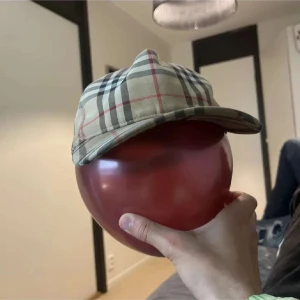 Burberry-inspirerad rutig keps - Snygg keps med klassiskt Burberry-inspirerat rutmönster i beige, svart, vitt och rött. Kepsen har böjd skärm och justerbar rem baktill. Perfekt accessoar för att lyfta din outfit med en tidlös och trendig vibe.