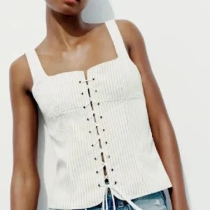 Vit korsett-topp med snörning - Snygg vit korsett-topp med breda axelband och snörning framtill. Toppen har en lätt ribbad struktur och fyrkantig ringning, perfekt till jeans eller kjol. Fräsch och trendig look för dig som gillar stilrena detaljer.