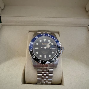 Seiko Marine Master automatisk klocka - Snygg Seiko Marine Master automatisk klocka med blå och svart vridring, jubilee-länk i silverfärgat stål och svart urtavla med tydliga index. Klockan har datumfönster och robust design, perfekt för dig som gillar stilren och sportig look.