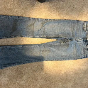 Blåa bootcut jeans från Gina Tricot - Säljer ett par ljusblå jeans från Gina Tricot med råa, fransiga benslut. Jeansen har klassisk femficksdesign, låg midja och bootcut för en chill och trendig look. Perfekta till sneakers eller boots. 