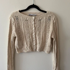 Beige stickad tröja Zara - Superfin beige stickad tröja från Zara med coola hålstickade detaljer och klädda knappar framtill. Croppad modell med lång ärm och bred ribbad kant vid halsen. 