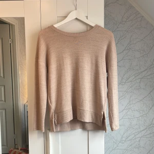 Beige stickad tröja från Holly's XS - Beige stickad tröja från Holly's i storlek XS. Tröjan har rund halsringning, ribbade muddar och slitsar i sidorna för en chill look. Perfekt för lager-på-lager under hösten eller vintern. Enkel att matcha med jeans eller kjol.