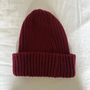 Vinröd ribbstickad mössa - Snygg vinröd mössa med bred uppvikt kant och ribbstickad struktur. Perfekt för kalla dagar och enkel att matcha med olika outfits. Mjuk och skön passform som sitter bra på huvudet.