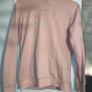 Ljusrosa hoodie Peak Performance - Säljer en ljusrosa hoodie från Peak Performance med broderad logga framtill. Tröjan har huva, känguruficka och långa ärmar. Mjuk insida och ribbade muddar vid ärmslut och nederkant. Använd ett fåtal gånger. Strl 160 men passar som en XS. 