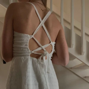 Vit kort sommarklänning med knytning i ryggen - Superfin vit kort klänning med smala axelband och öppen rygg med snygg snörning. Klänningen har en lätt strukturerad yta och v-ringad front. Perfekt för varma dagar och passar även vid finare tillfällen🙌🏼