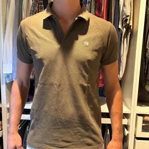 Olivgrön pikétröja från Scotch & Soda - Snygg olivgrön pikétröja med klassisk krage och två knappar framtill. Tröjan har korta ärmar och en liten diskret logga på bröstet. Perfekt för en clean och sportig stil. Nypris 699. 