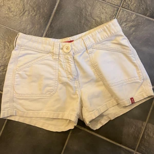 Vita shorts med fickor - Snygga lågmidjade vita shorts. De har två stora framfickor och två bakfickor med lock och knapp. Perfekta för sommardagar och har en normal passform med midwaist. Stängs med knapp och dragkedja framtill. PRIS KAN ALLTID DISKUTERAS!!