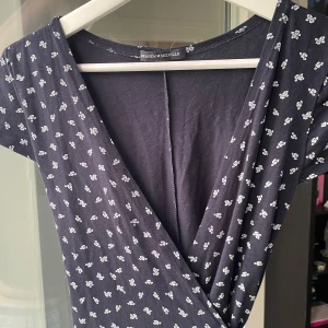 Mörkblå blommig omlottklänning Brandy Melville - Supersöt mörkblå omlottklänning från Brandy Melville med små vita blommor. Klänningen har korta ärmar, v-ringning och knyt i midjan. Tillverkad i 100% bomull, perfekt för en chill och trendig look. Passar bäst storlek 34-38. 