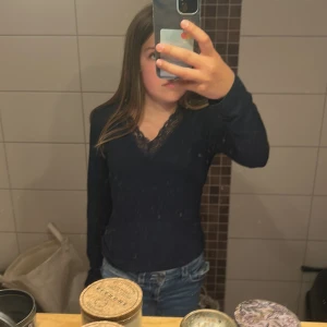 Mörkblå långärmad topp med spets - Supersnygg mörkblå långärmad topp från Gina Tricot med v-ringning och fina spetsdetaljer vid halsen. Perfekt att styla med jeans eller kjol för en trendig look. Skön passform och mjukt material.